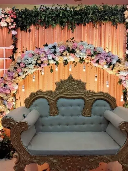 A classic stage setup for a wedding or engagement. The design features a beautiful floral arch in pastel shades, elegant draping, and a vintage-style sofa, creating a romantic and picture-perfect focal point for the event.