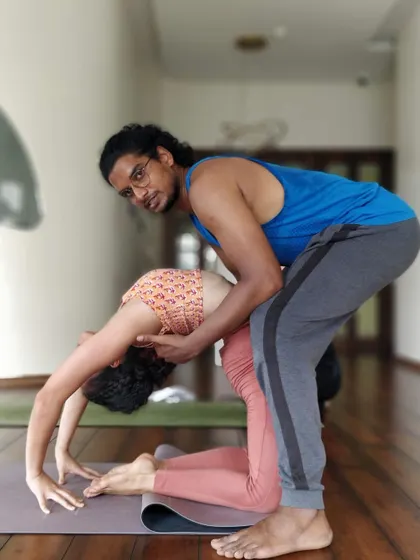 An instructor helps a student deepen their Ustrasana (Camel Pose), focusing on opening the chest and shoulders safely.