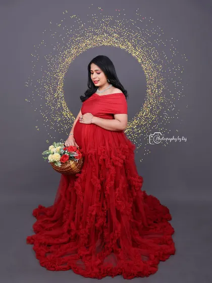 A lovely studio portrait of a mother-to-be in a red ruffled gown, holding a basket of flowers.