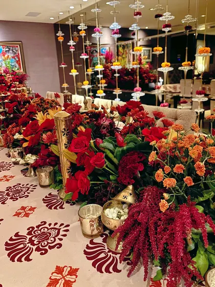 A luxurious Diwali tablescape, featuring a runner of red and orange flowers, traditional brass lamps, and hanging floral strings.