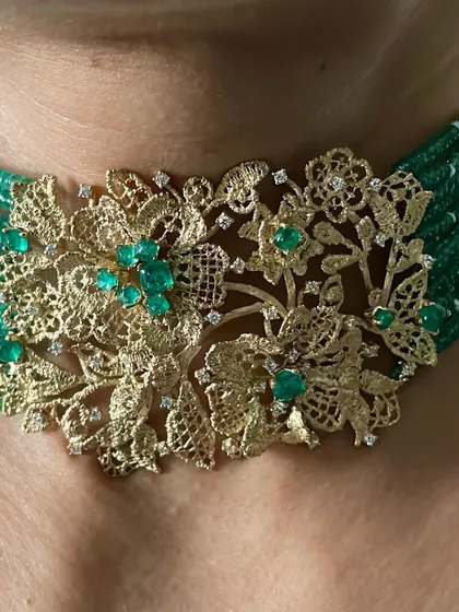 A close look at a handcrafted choker, where lace like 18k yellow gold meets the deep green of natural emeralds and the sparkle of diamonds. This piece is designed to sit gracefully, making a statement of pure elegance.