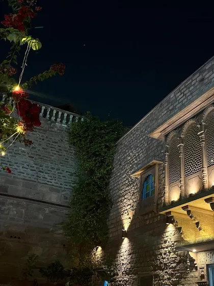 A beautiful historic building in Jodhpur at night. The way the lighting highlights the architecture and the surrounding plants creates a warm and inviting scene.
