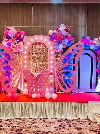 A beautiful stage setup for a baby girl's naming ceremony with a butterfly theme. The decor features large pink butterfly wings and arches, creating a soft and celebratory atmosphere.