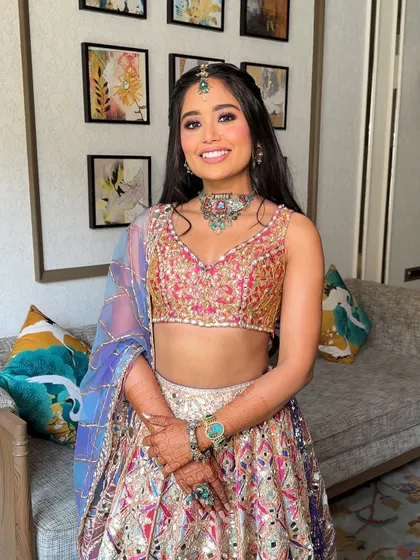 A fun and festive Mehendi look featuring a half-up braided crown and bouncy curls, adorned with small mirror accessories that match the bride's Abhinav Mishra lehenga.