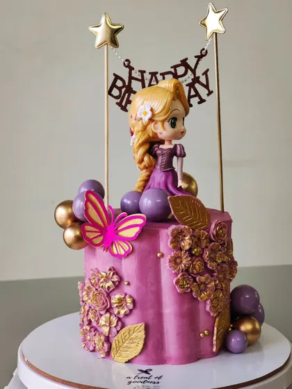 A Rapunzel-themed cake with a unique scalloped shape. The design is adorned with golden floral details, a butterfly, and a cute Rapunzel figurine.