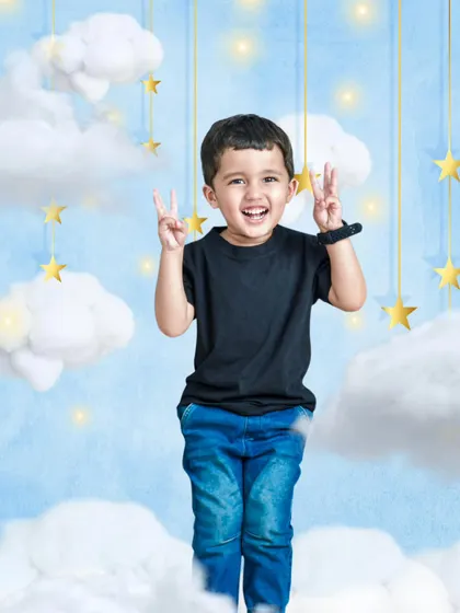 A joyful boy stands amidst a dreamy backdrop of clouds and stars, making a peace sign with both hands, perfectly capturing the theme of reaching for the stars.