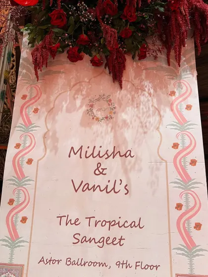 A welcome sign for a "Tropical Sangeet," adorned with deep red flowers, setting the theme for the evening.