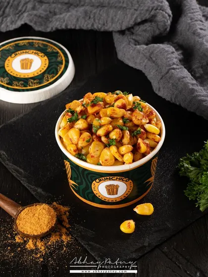 This shot of spiced corn uses a dark and moody theme to emphasize the rich spices and textures. The scattered masala and parsley add a sense of action and flavor to the composition.