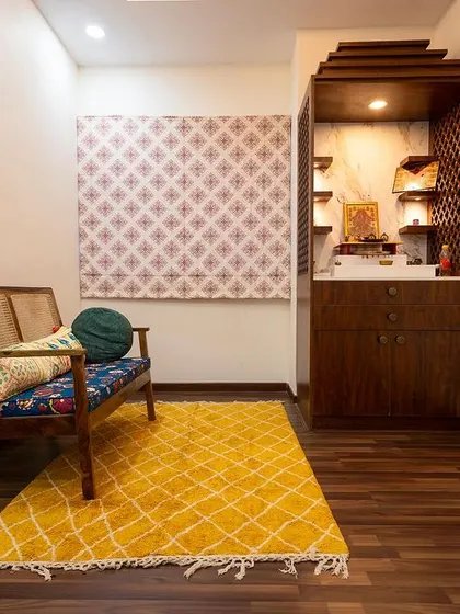 A cozy corner in Nisha and Arun's home dedicated to prayer and reflection. The compact wooden pooja unit is complemented by a comfortable bench and colorful decor.