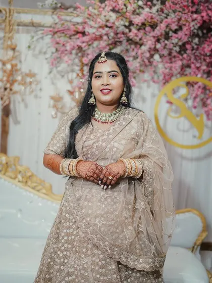 A lovely portrait of the bride in her elegant beige lehenga, standing in front of the engagement stage. Her hands are clasped, showcasing her beautiful mehndi and bangles.