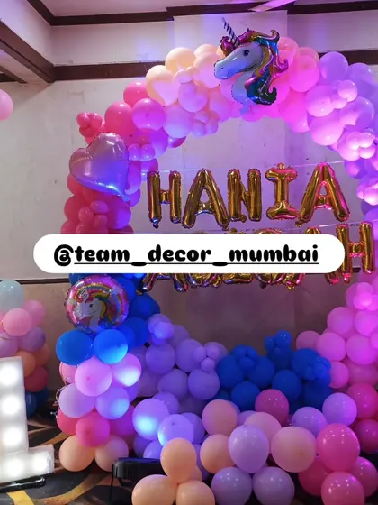 A magical unicorn-themed first birthday party. The decor is built around a massive circular balloon arch in vibrant rainbow colors, with a unicorn foil balloon at the top and a light-up marquee number '1'.