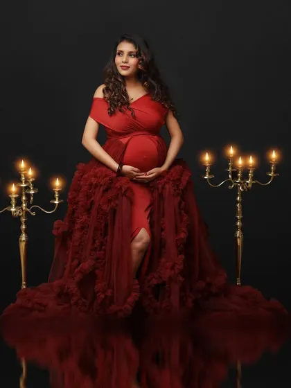 A vision in red. This mom-to-be is seated amidst candelabras in a voluminous red gown, her reflection captured on the floor for a stunning effect.