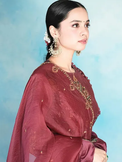 A side profile of Nitanshi Goel, showcasing the movement and detail of the handcrafted gold jhumka earrings. They are designed to be statement pieces for special occasions.