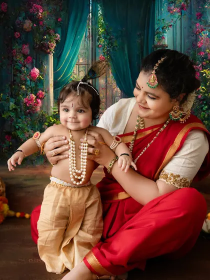 A magical moment with a smiling baby Krishna against an enchanting floral and curtained backdrop.