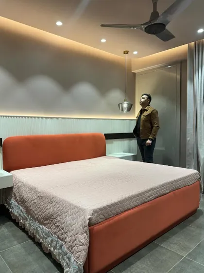 A finished bedroom with a vibrant orange upholstered bed. The headboard is set against a fluted panel wall with soft backlighting.