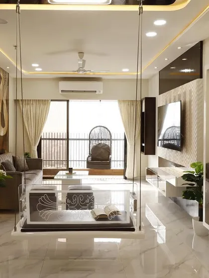 A shot of the Malad living room, focusing on the transparent acrylic swing that serves as a centerpiece. The design includes a custom TV unit and a mirrored storage cabinet, reflecting light and enhancing the room's spaciousness.