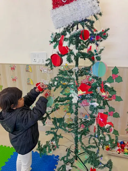 A toddler carefully places an ornament on the Christmas tree, practicing fine motor skills while participating in a festive tradition.