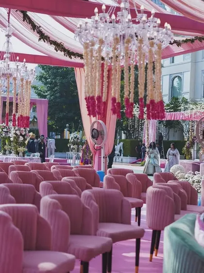 A view of the guest seating area, featuring rows of elegant pink velvet chairs. The entire space is under a canopy of pink fabric, with beautiful floral chandeliers creating a luxurious atmosphere.