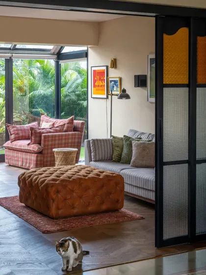 A family room in the Calcutta home, where a comfortable, oversized ottoman invites you to put your feet up. The sliding doors with fluted glass add a touch of vintage charm and separate the space without blocking light.
