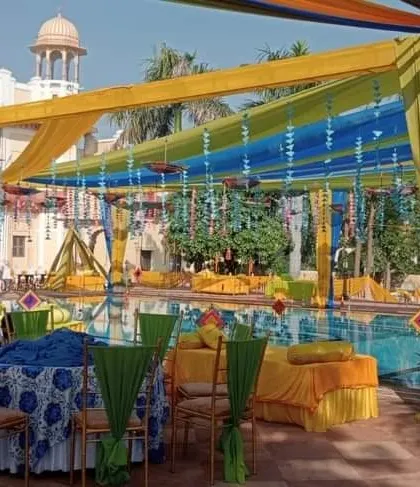 A poolside Haldi decoration with a canopy of colorful drapes and hanging ornaments, creating a festive atmosphere for the daytime event.