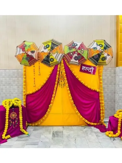 A compact and vibrant Haldi corner setup, perfect for smaller spaces. It features a bright yellow and magenta backdrop, decorative umbrellas, and fun directional signs to guide guests.