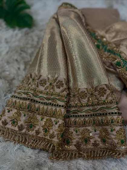 A close-up of the sleeve of the beige blouse, highlighting the intricate embroidery with gold, green, and black threads.