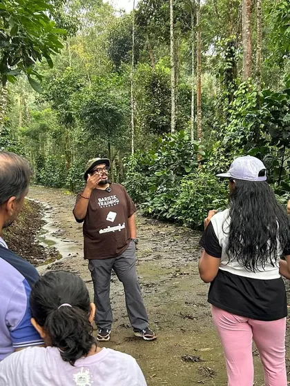 On the ground at a coffee farm, explaining the importance of shade-grown coffee to a group of visitors.