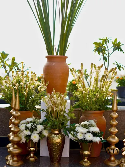 A beautifully curated corner with terracotta vases, golden candlesticks, and lush white blooms, bringing together earthy tones and metallic shine.