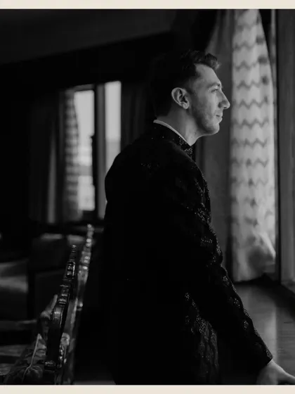 A moody, vintage-toned profile shot of the groom looking out a window, lost in thought before the ceremony.