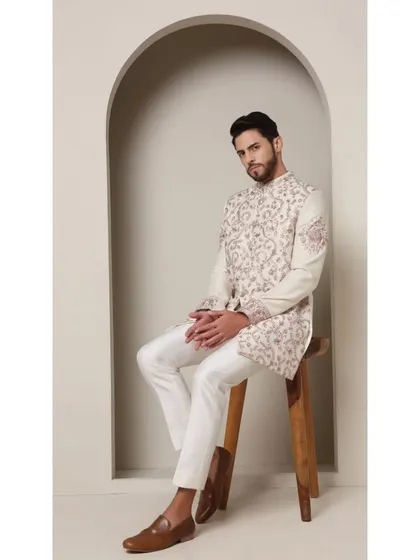 Seated pose in the 'Ivory Rose' bandhgala. This view shows the intricate jaal work across the body of the jacket and the clean fit of the accompanying white trousers.