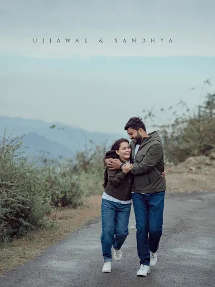 A happy, candid shot of a couple walking and laughing on a mountain road. Their matching jackets and relaxed posture give the photo a natural, authentic feel.