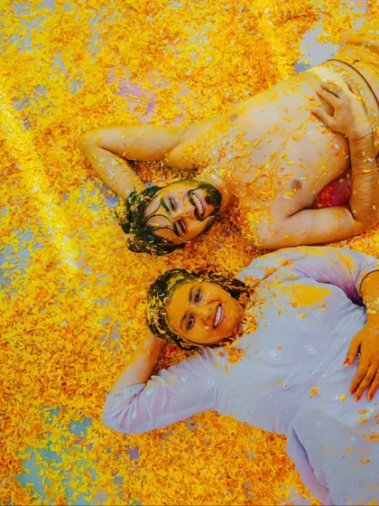 After the joyful chaos, a moment of rest. The couple lies in a bed of flower petals, smiling, a unique and artistic shot from their Haldi ceremony.