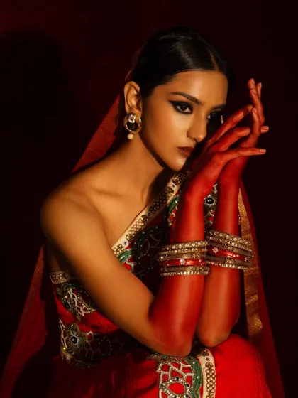 A dramatic and artistic bridal portrait. The use of red-stained hands (alta) and intense, moody lighting creates a powerful and traditional image with a modern feel.