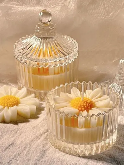 Two daisy candy jar candles, one with the lid on. These make for a very elegant and reusable gift.