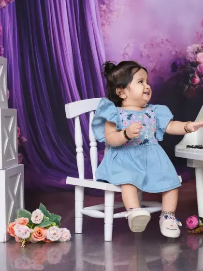 A baby girl reaches for the keys of a miniature piano, surrounded by flowers. This shot captures a moment of curiosity and discovery in a beautiful setting.