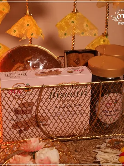 A golden wire basket hamper for Diwali, featuring a box of my classic almond biscotti, a dry cake, and jars of other delicious treats.