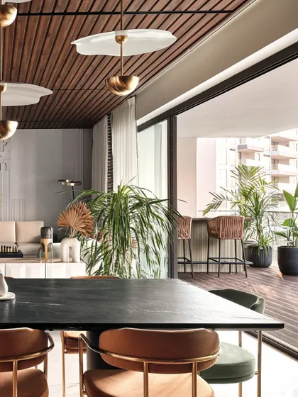 The dining area opens up to a spacious balcony with a bar, blurring the lines between indoor and outdoor living. The wooden ceiling continues throughout the space, creating a sense of warmth and cohesion.