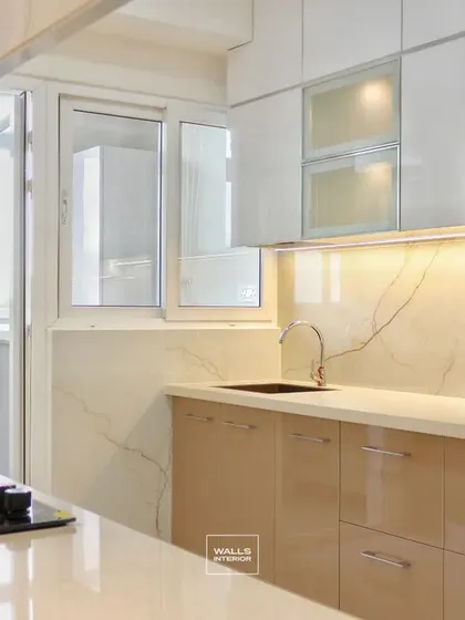This view shows the L-shaped layout of the beige and white kitchen, providing an efficient work triangle between the sink, hob, and refrigerator. The large window allows for ample natural light.