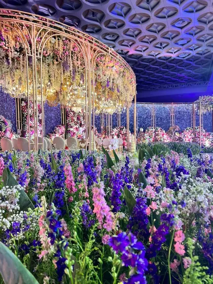 A garden of earthly delights. This reception stage is a floral masterpiece, with a structure completely enveloped in a sea of purple, pink, and white flowers, set against a sparkling backdrop.