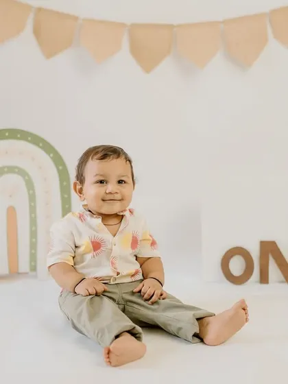 A cheerful first birthday setup with a boho rainbow theme. This little boy's smile shows he's having a wonderful time celebrating his big day.
