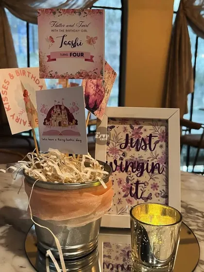 'Just wingin' it'. A cute and creative centerpiece for a fairy party, featuring themed cards, a framed sign, and a silver candle holder.