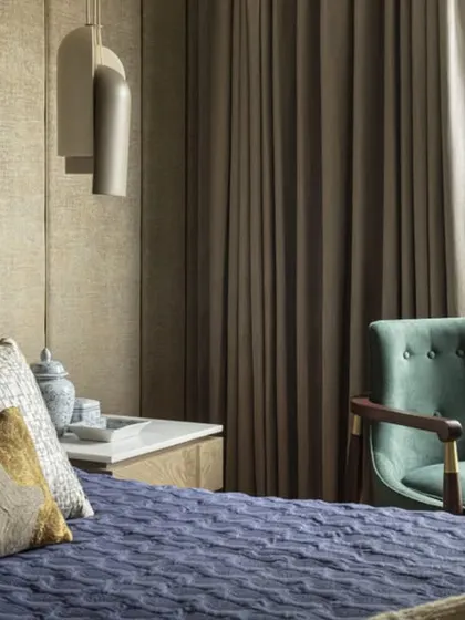 A corner of a bedroom at the Jor Bagh Residence, where a comfortable teal armchair sits by a large window. This space is designed as a quiet reading nook, with natural light and views of the greenery outside.