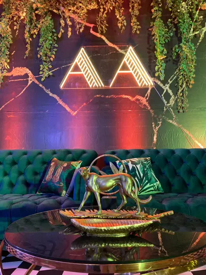 A custom neon monogram for the couple is set against a dark, textured wall with hanging vines, blending modern personalization with the wild theme.