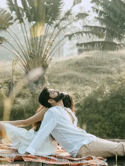 A relaxed, full-body shot of the couple on a picnic by the water, with large traveler's palms in the background. It has a very serene and tropical feel.