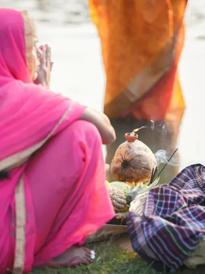 A devotee kneels by the water's edge with her offerings during Chhath Puja. The atmosphere is one of quiet reverence and deep faith.