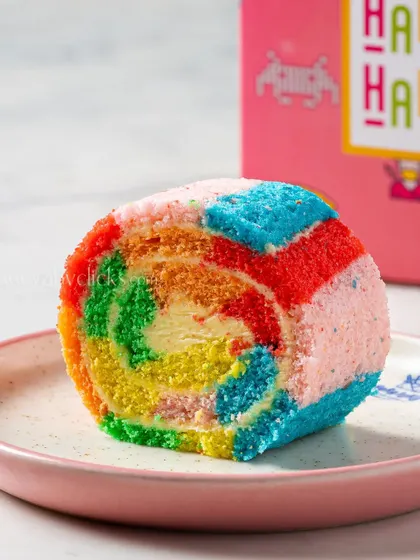 A colorful rainbow Swiss roll, sliced to reveal its vibrant layers, making for a playful and eye-catching dessert photograph.