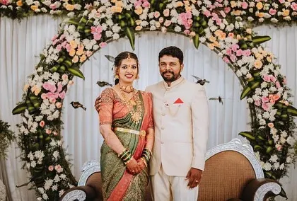 A lovely portrait of a couple at their engagement, standing before a circular arch decorated with soft pink and white flowers.
