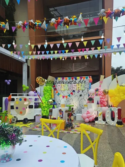 A wide shot of a colorful art-themed party. The setup includes a large backdrop for coloring, a paint-truck prop, and tables set for creative activities, making it an artist's dream party.