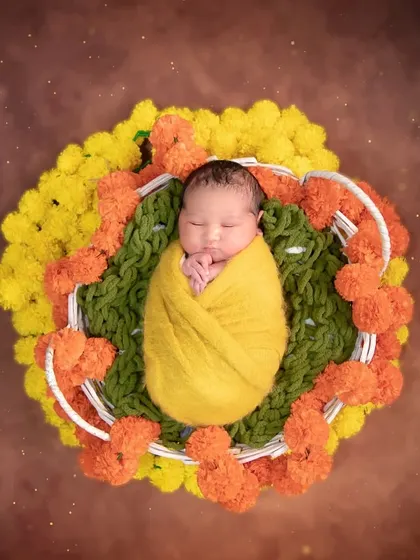 An overhead shot of the Diwali setup. The baby is the center of a beautiful rangoli made of orange and yellow marigolds, celebrating the festival of lights.