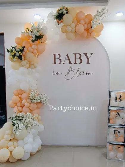 A "Baby in Bloom" themed baby shower decor for an intimate home setting. This setup features a beautiful balloon arch in peach and white tones with floral accents.